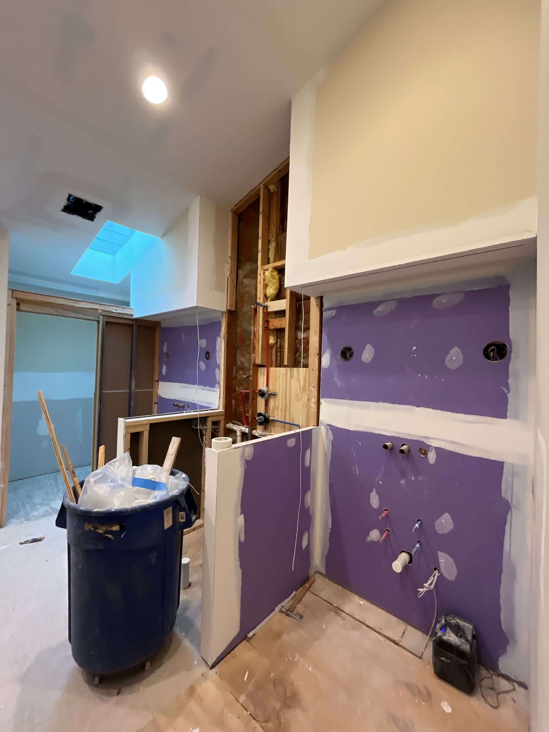 Partially renovated kitchen with purple drywall, exposed studs, and a blue trash can on the floor