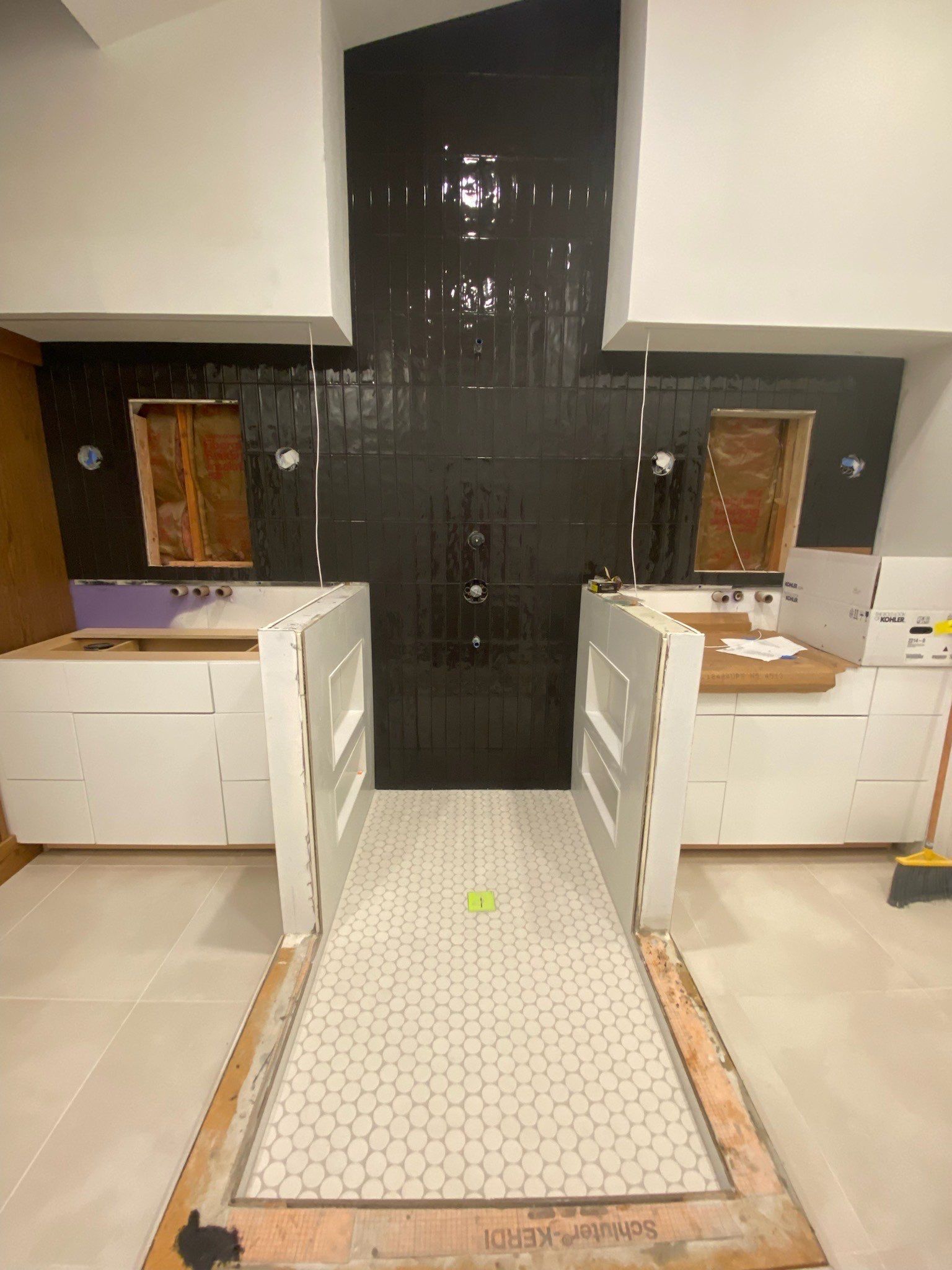 Small bathroom with white cabinets, open vanity doors, and a dark tiled accent wall.