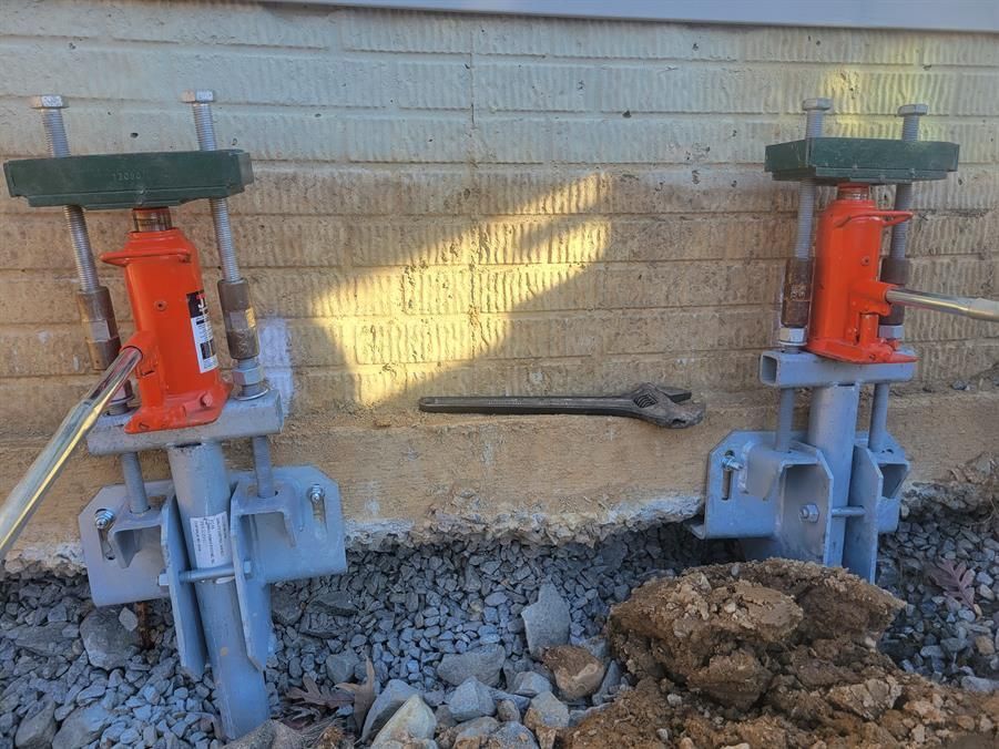 Two hydraulic jacks are sitting next to each other in front of a brick wall.