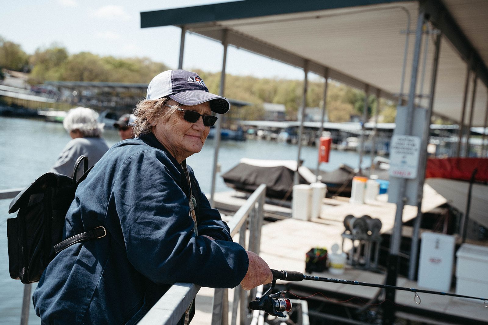 Woman in sunglasses and hat fishing from a dock on a sunny day.