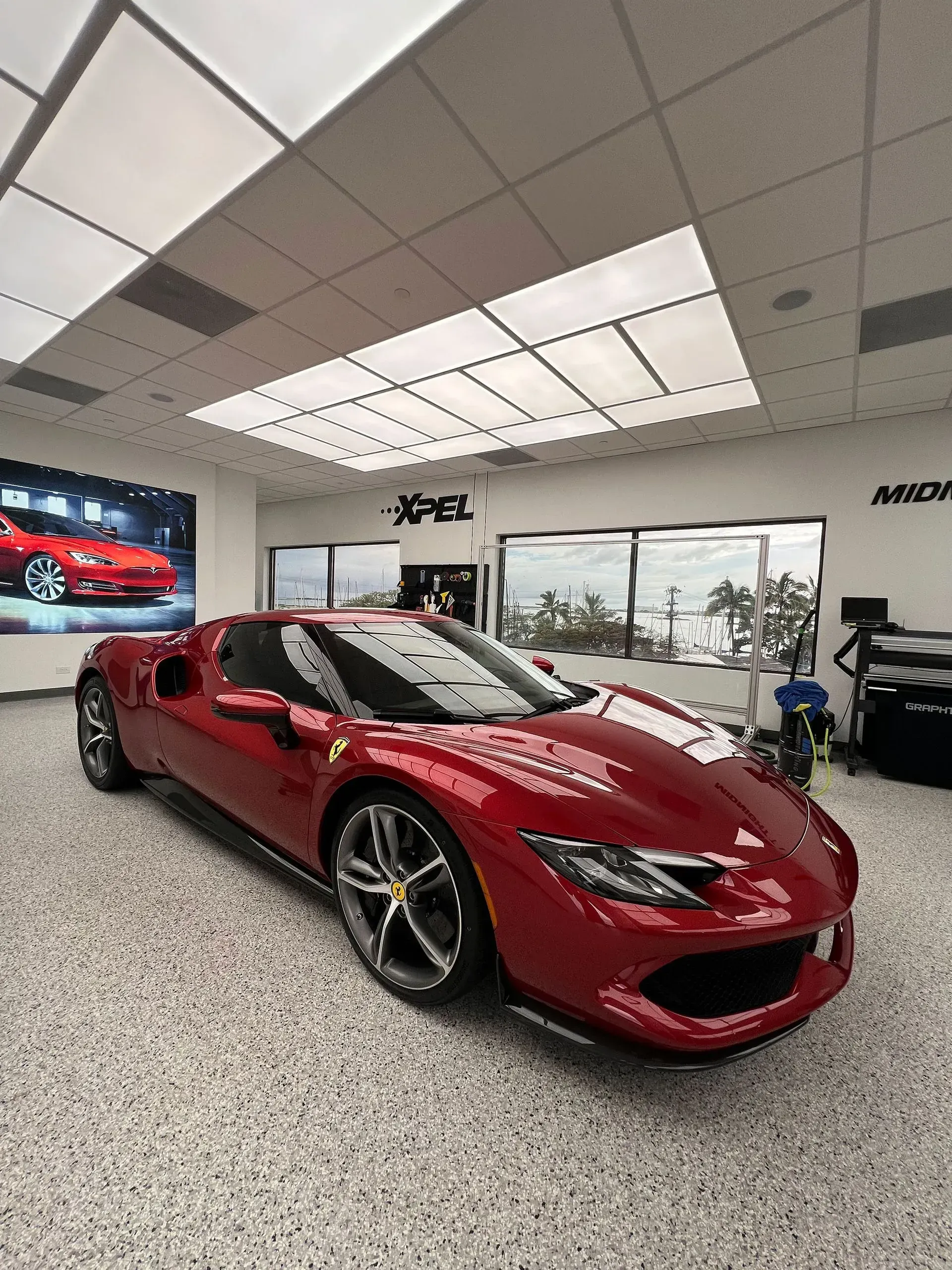 Red Ferrari sports car in a showroom with a speckled floor and large windows.
