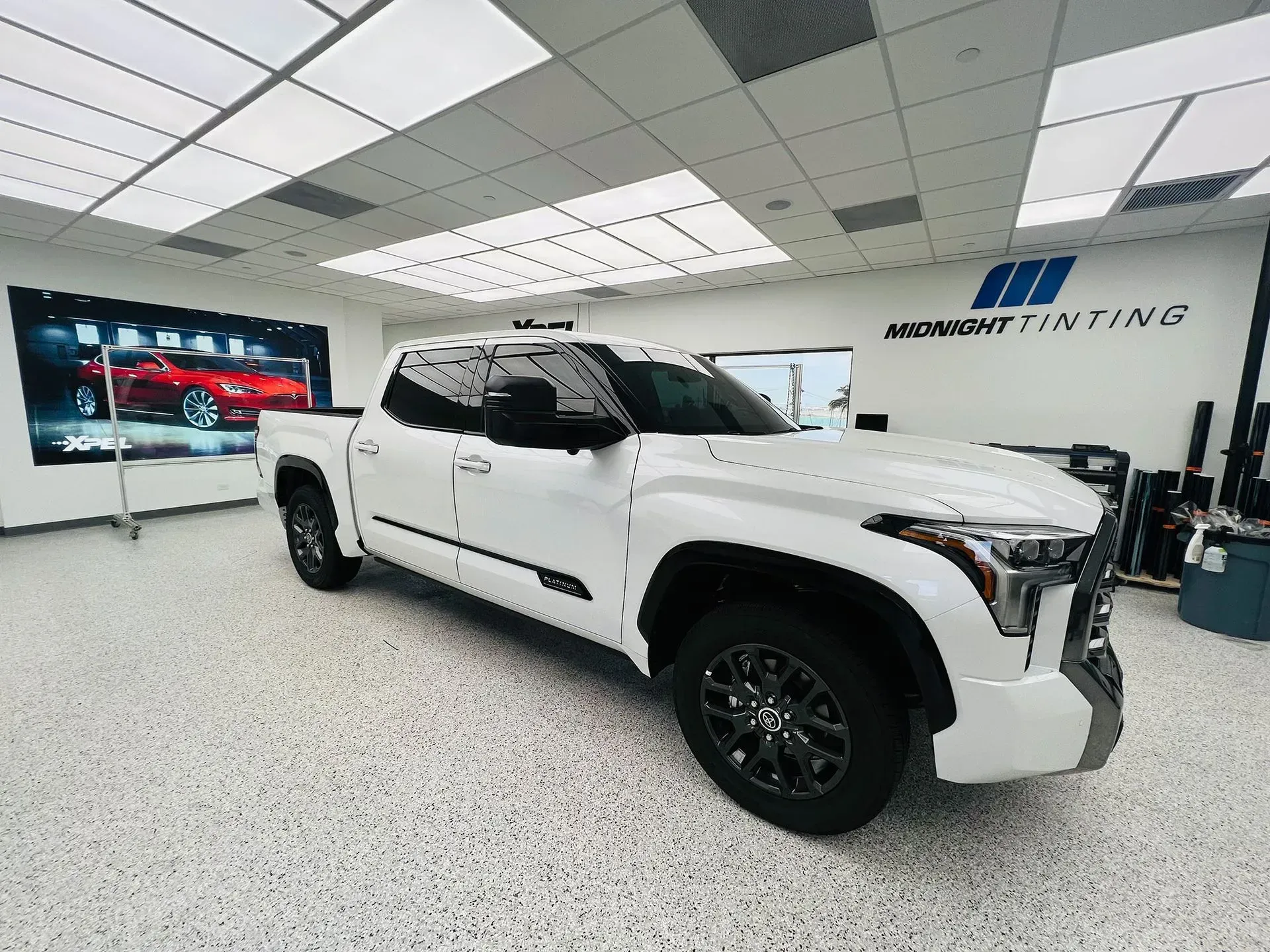 White Toyota Tundra pickup truck in a shop, windows tinted, black wheels, against a backdrop with a Midnight Tinting sign.