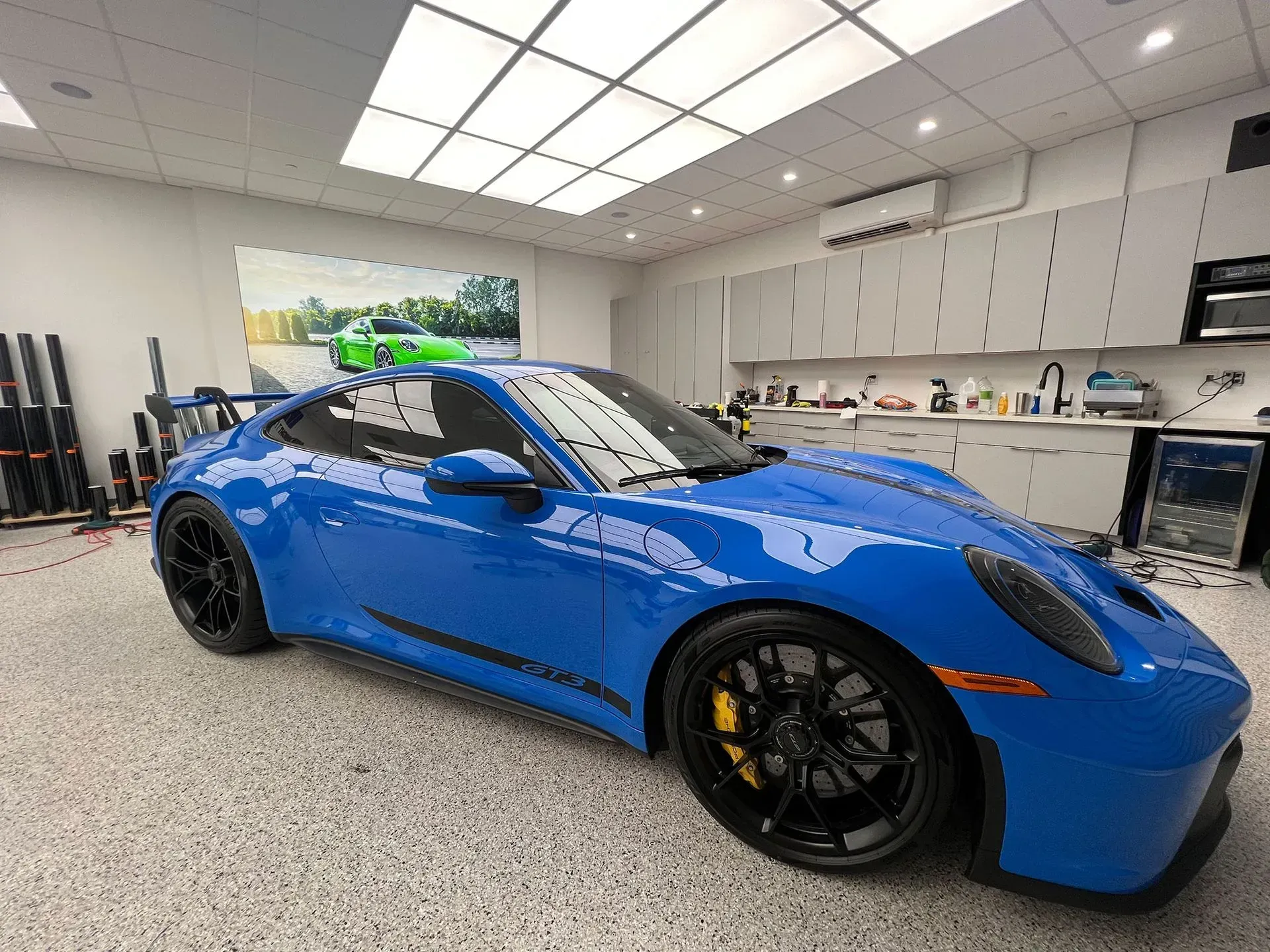 Blue Porsche sports car in a garage with black rims and yellow brake calipers.