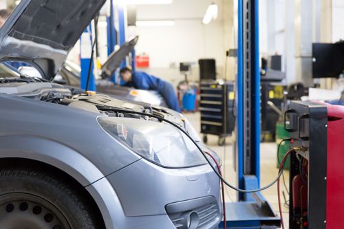 Silver car charging in an auto repair shop with hood open