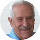Smiling elderly man with white hair and mustache in a blue shirt, shown in a circular portrait