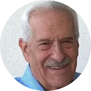 Smiling elderly man with white hair and mustache in a blue shirt, shown in a circular portrait