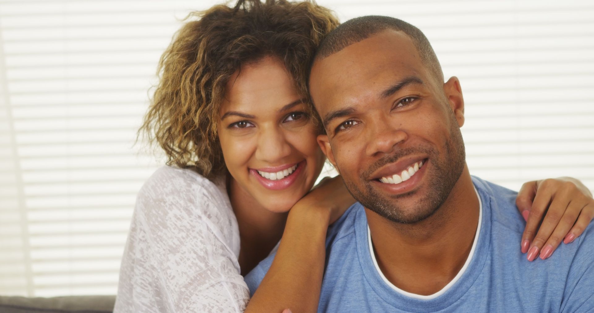Smiling couple, woman with arm around man, posing together indoors.