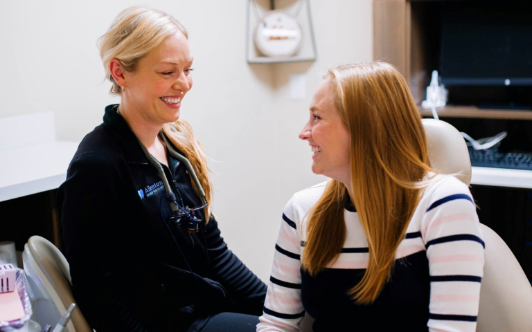 Smiling patient in dentist chair, dentist and assistant smiling, dental office.