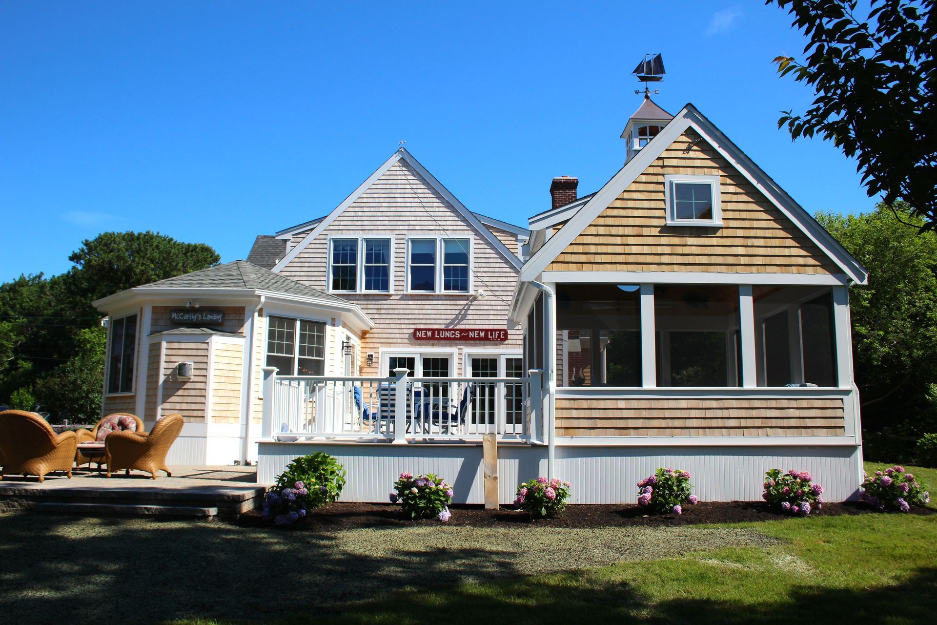 Coastal home with cedar shake siding, porch, and deck on a sunny day