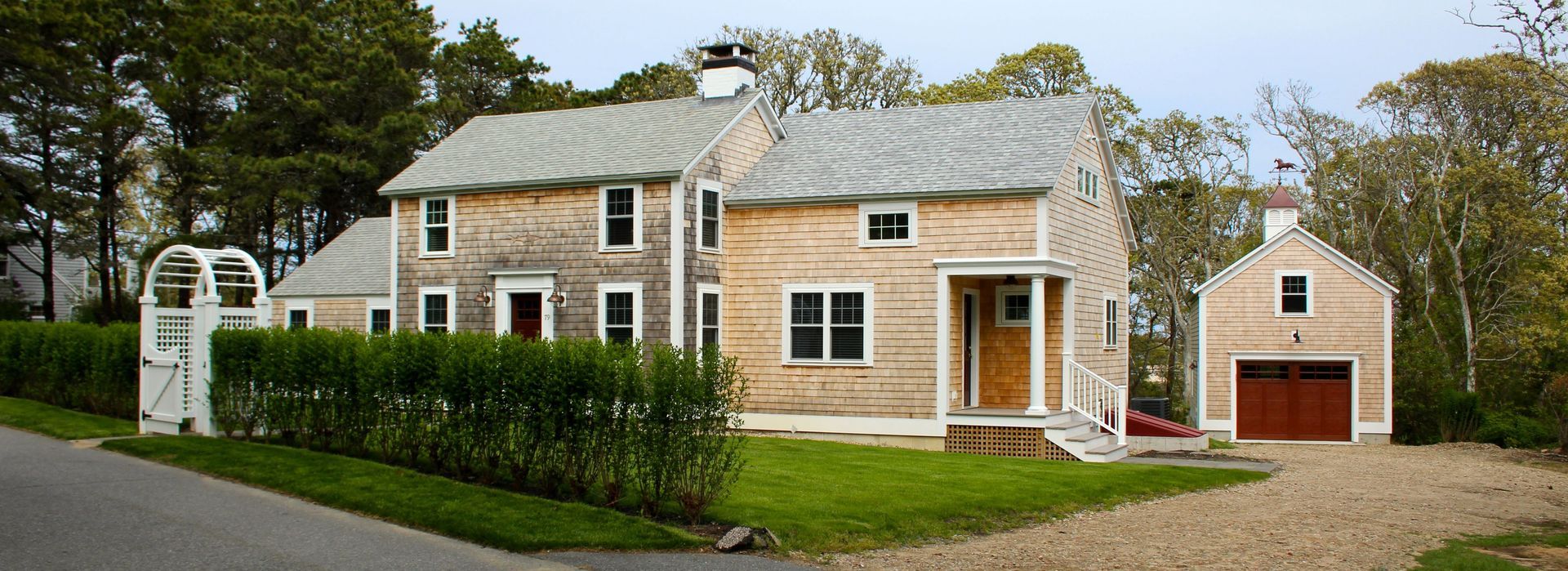 A weathered, two-story wooden house with a garage and manicured lawn in front