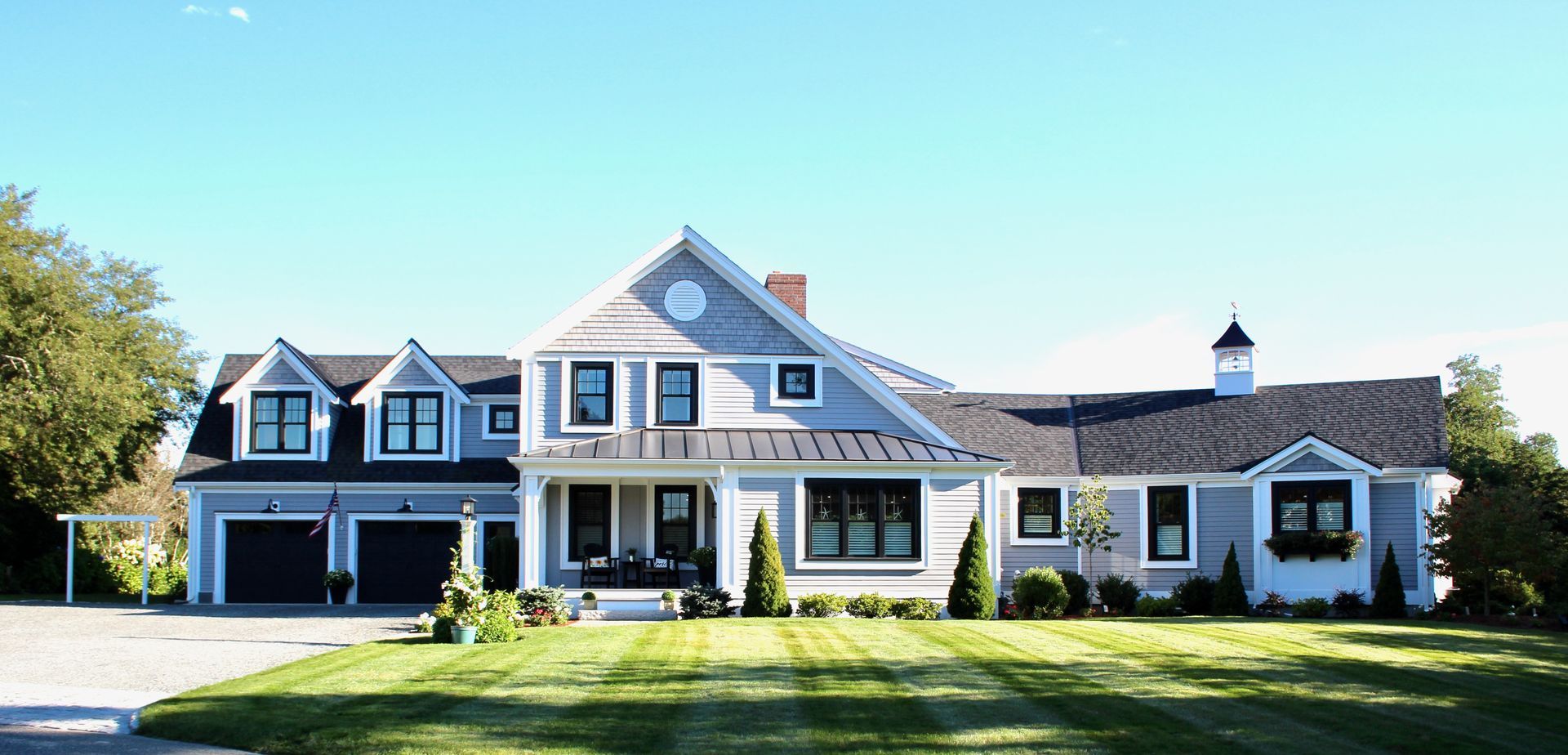 A light blue, two-story house with a large lawn, and a bright blue sky