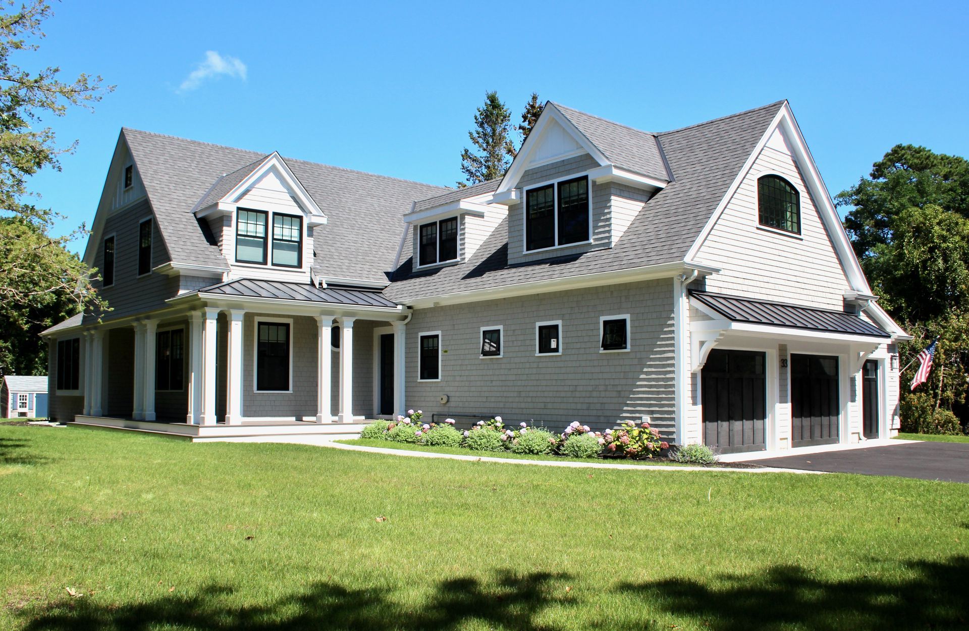 Two-story gray house with white trim, columns, and a dark garage door. Blue sky and green grass