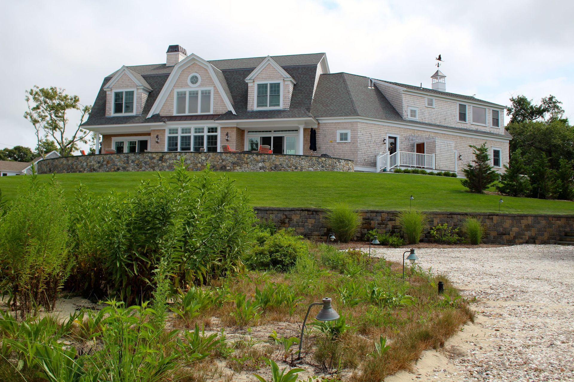 Pink and white house with dormers atop a grassy hill, near a shore