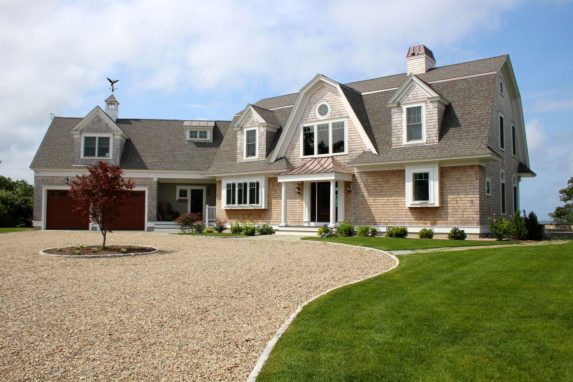 House with shingle siding, gravel driveway, and green lawn under a blue sky