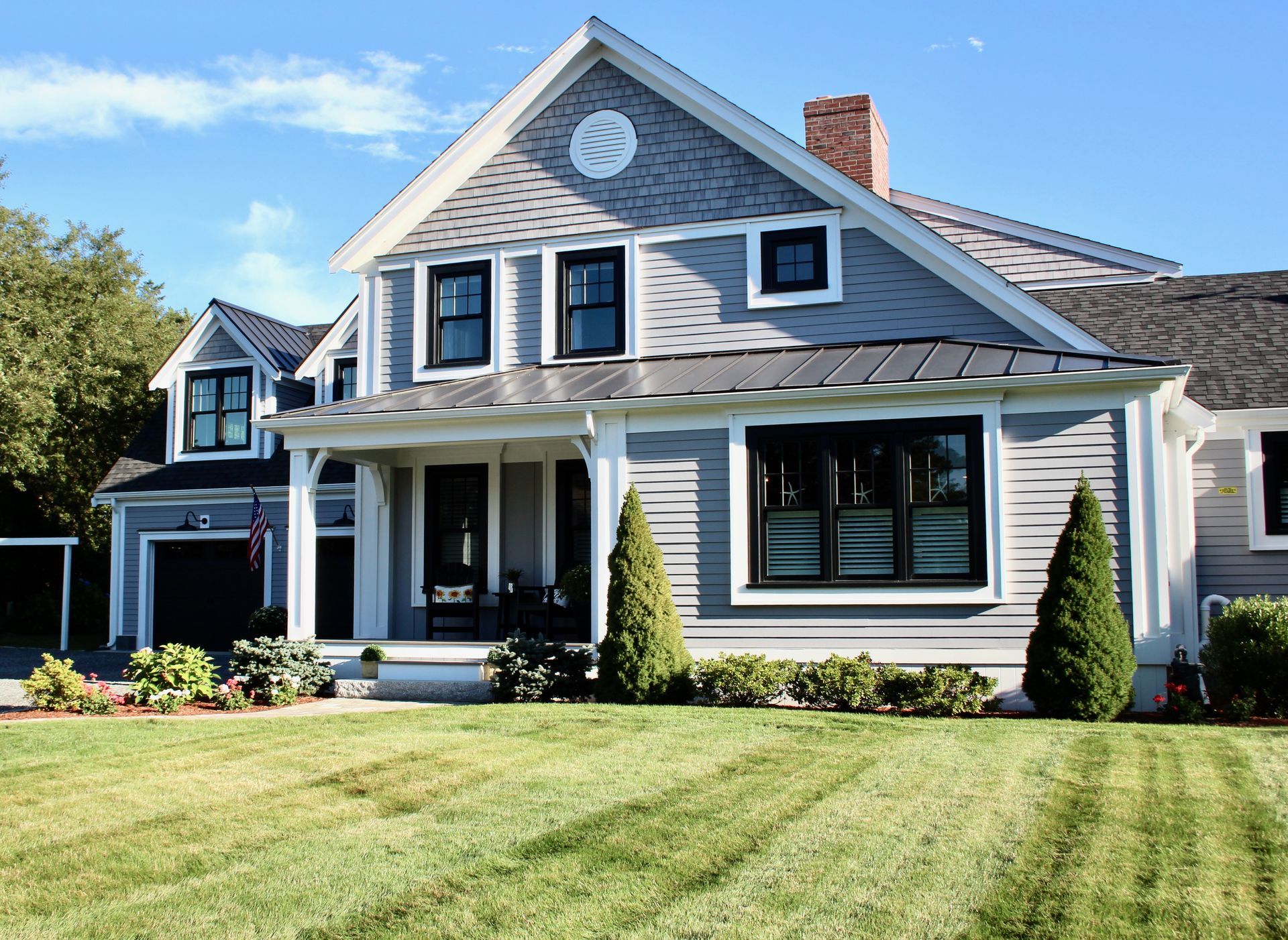 Gray house with white trim, black windows, and green lawn under a blue sky