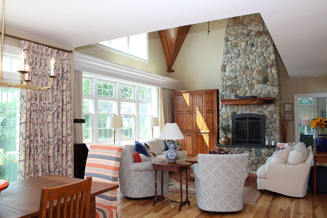 Living room with stone fireplace, window, two patterned armchairs, sofa, hardwood floors.