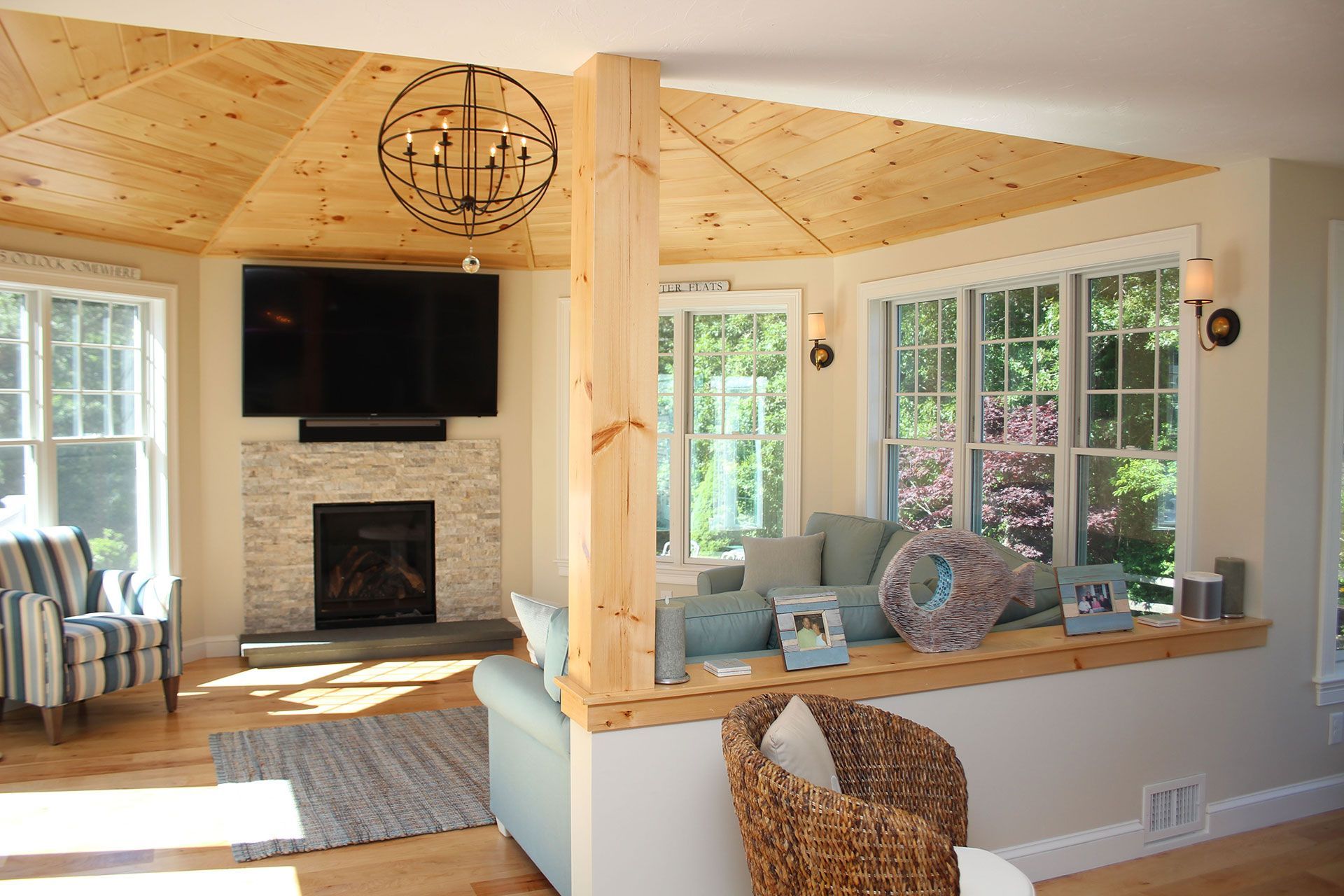 Living room with light wood ceiling and floors, fireplace, TV, and seating area with windows.