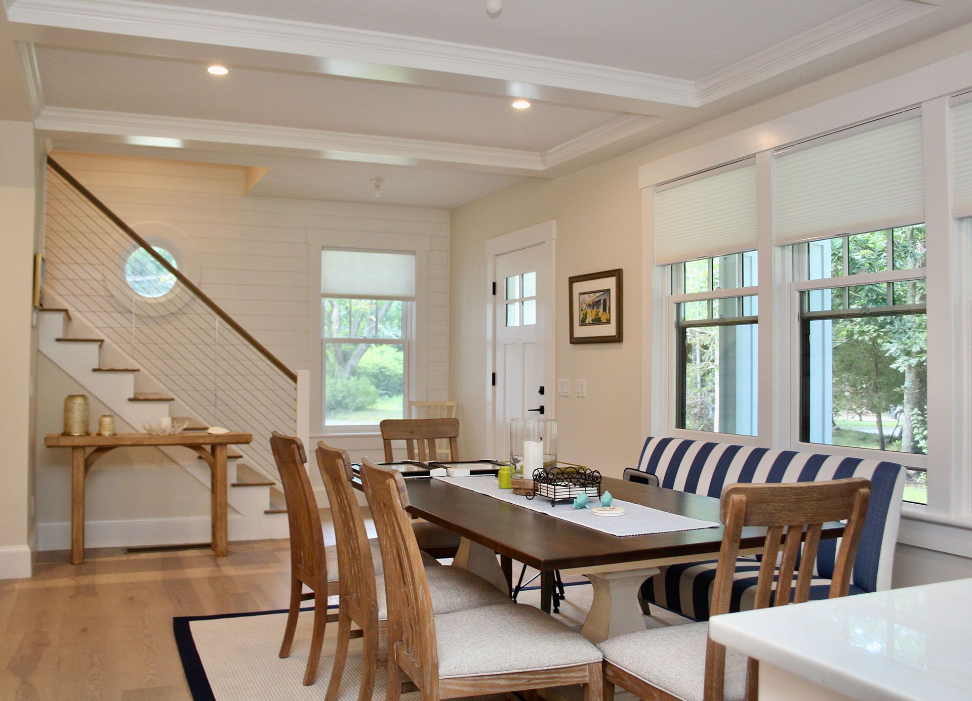 Dining room with a wooden table, striped bench, and staircase.