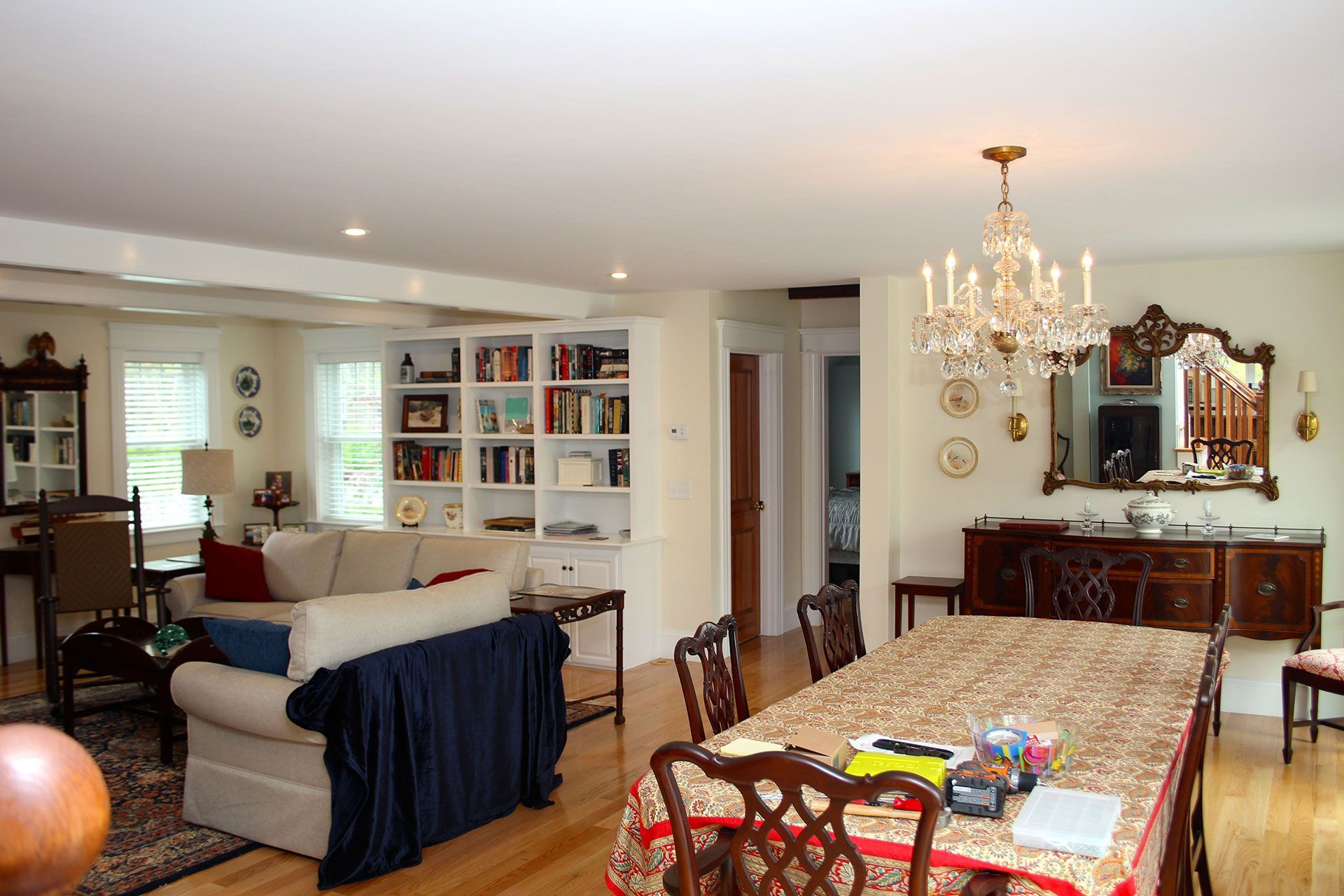 Open concept living and dining area. Light-colored walls and hardwood floors. Couch, table, buffet, and chandelier present.