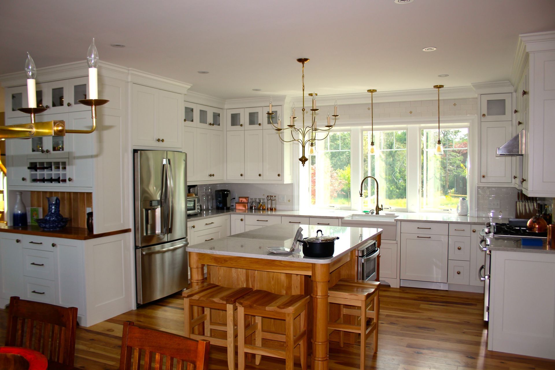 Spacious white kitchen with a wooden island, stainless steel appliances, and large windows overlooking a backyard