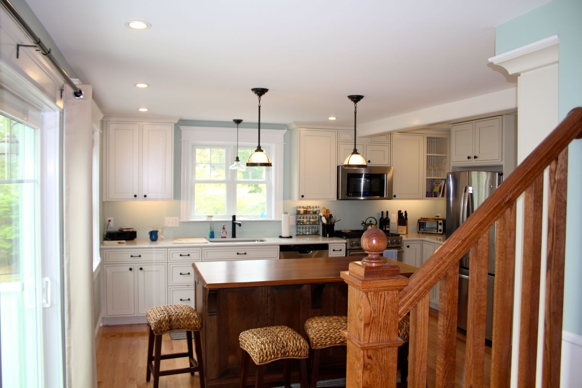 Kitchen with white cabinets, wood island, stools, and a staircase