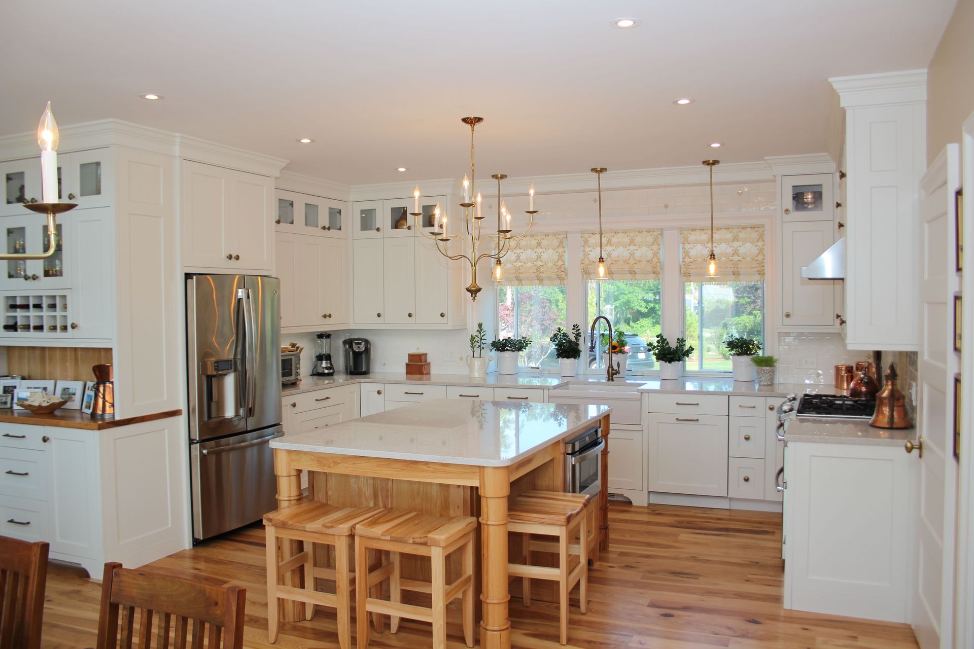 White kitchen with island, wood floors, stainless steel appliances, and pendant lighting