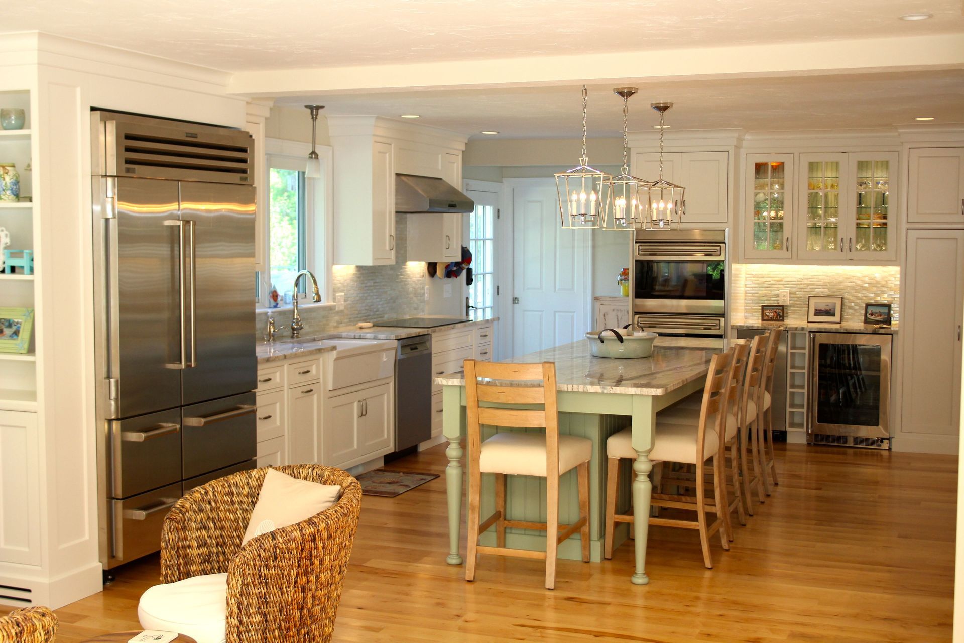 Spacious white kitchen with stainless steel appliances, island, and bar stools; light wood floors