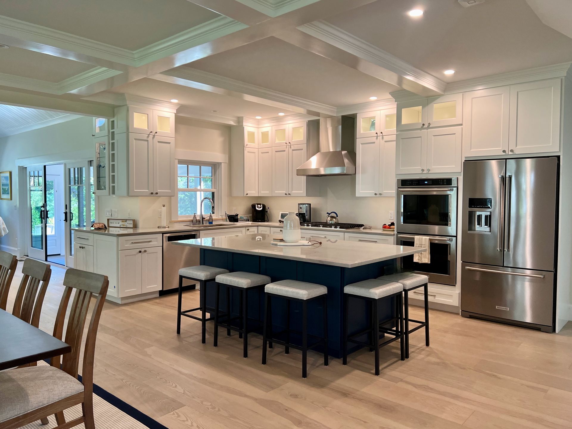 Bright, modern kitchen with white cabinets, navy island, stainless steel appliances, and light wood floors