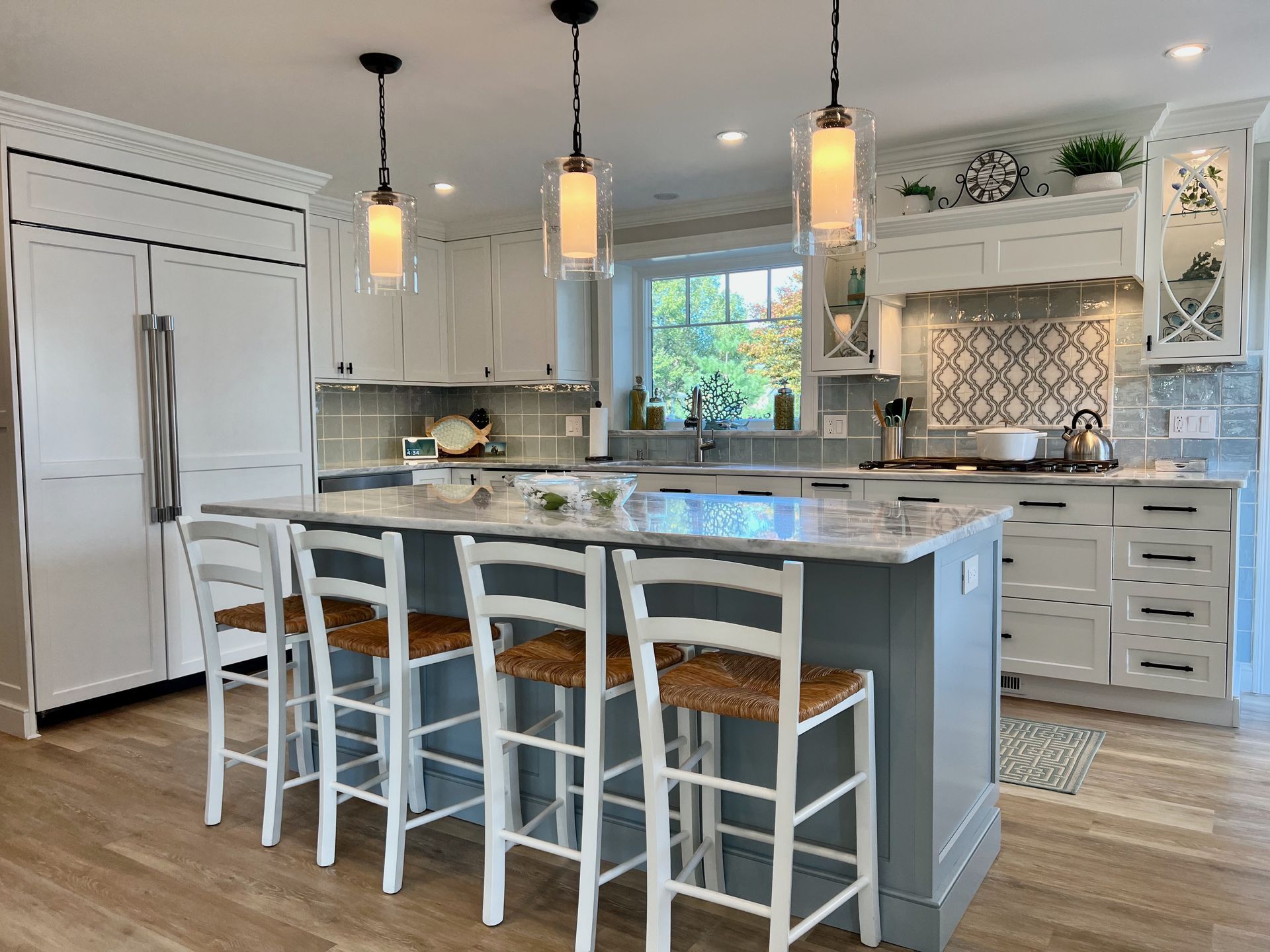 Spacious white kitchen with gray island, light wood floor, and pendant lights over the island seating