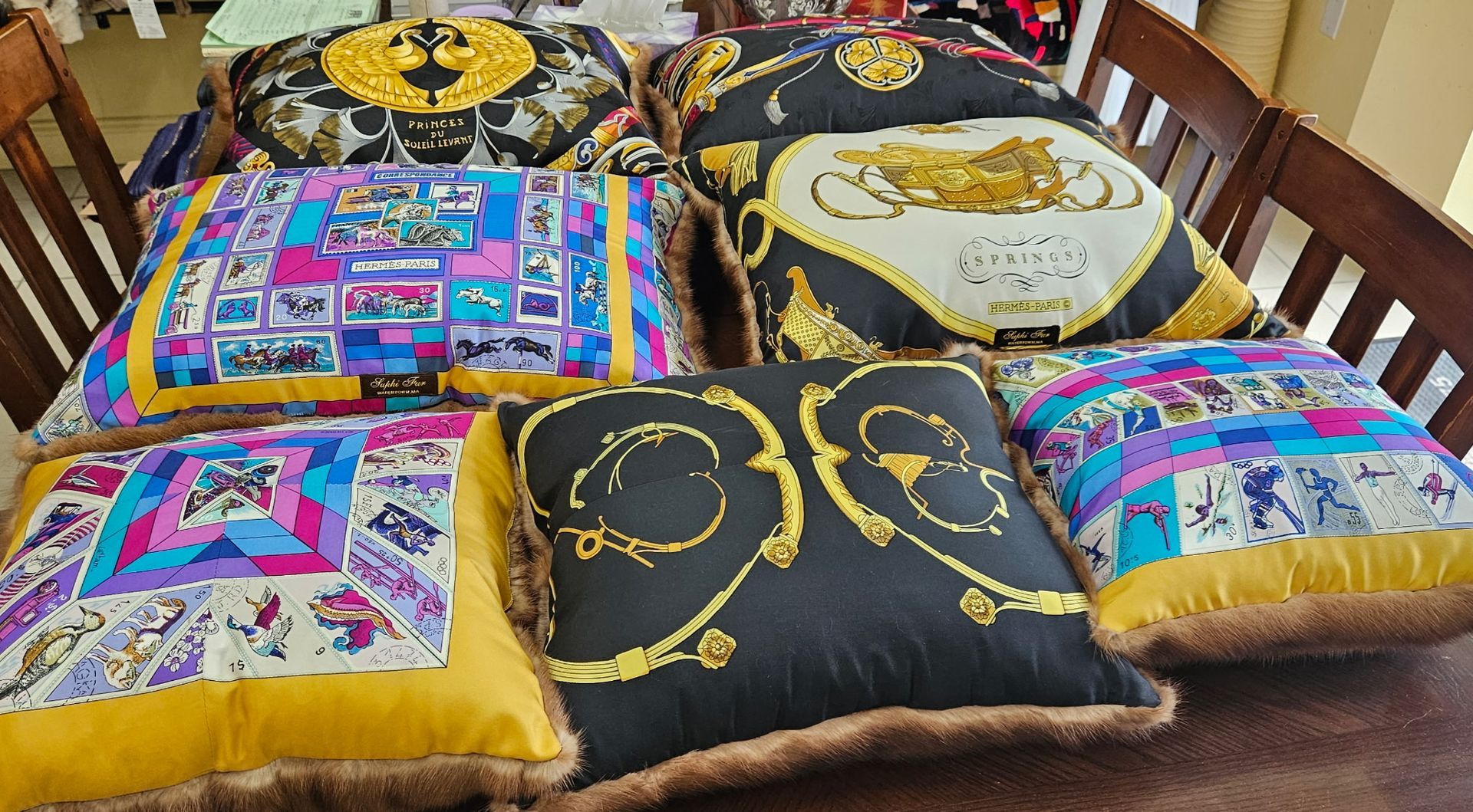 Colorful patterned cushions arranged on a bed, featuring gold, black, white, and pink designs.