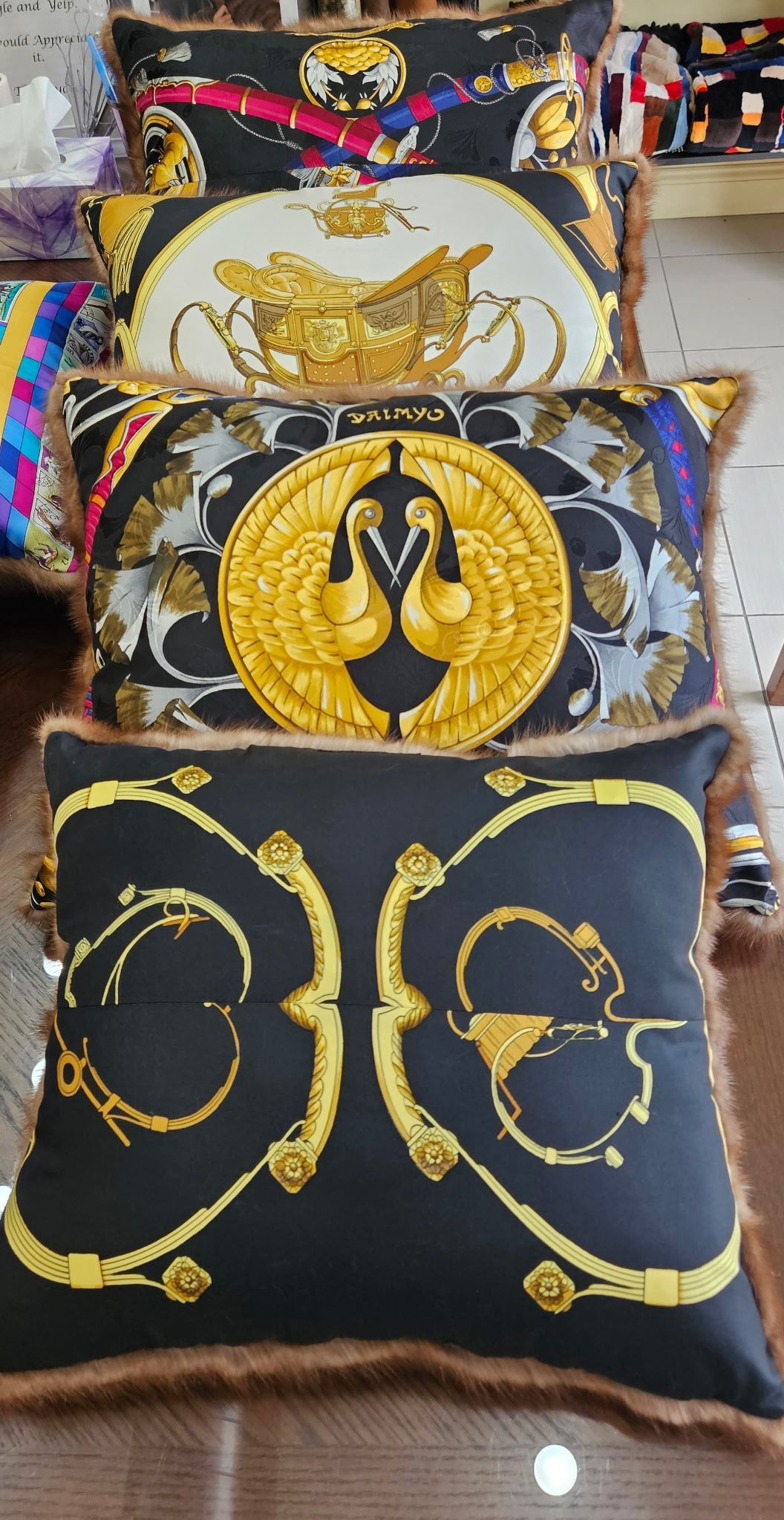 Three decorative cushions with gold black ornate patterns, stacked vertically on a display shelf
