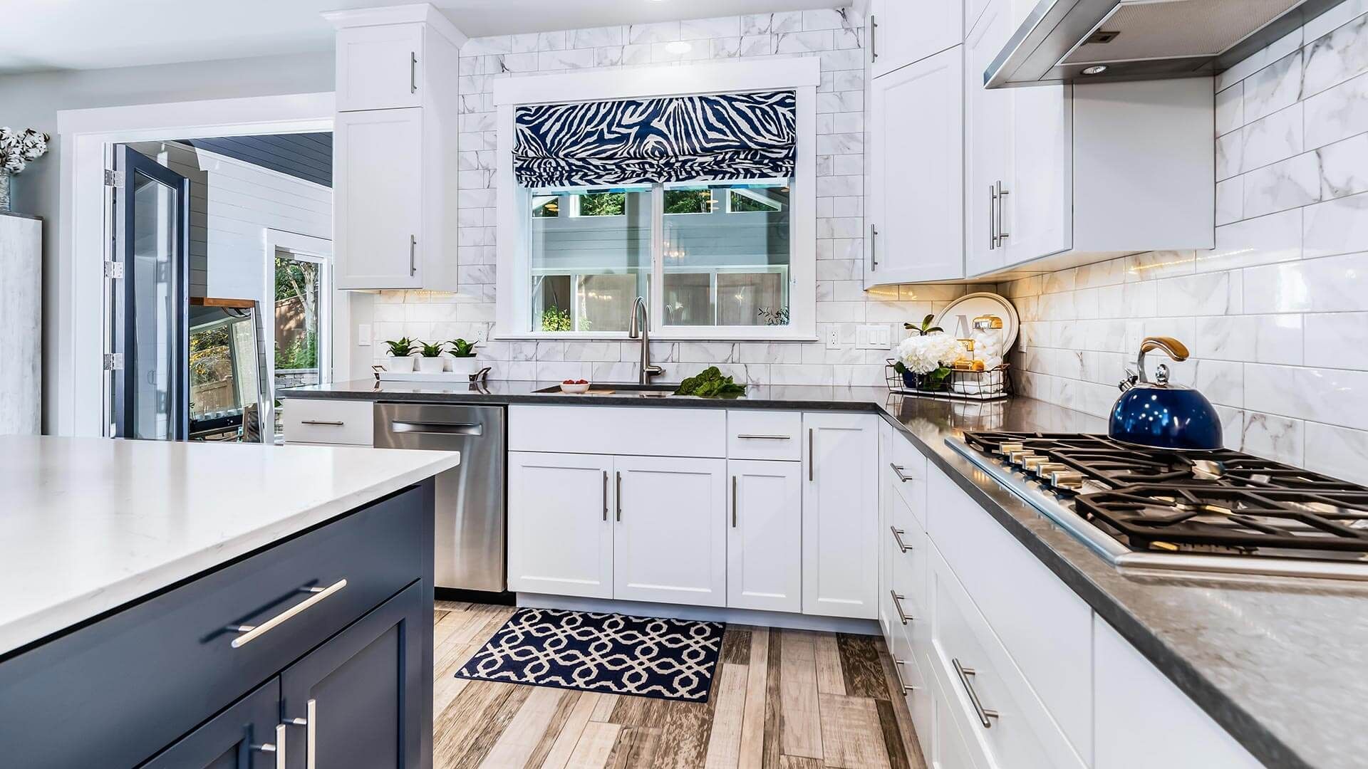 A kitchen with white cabinets , stainless steel appliances , a stove and a sink.