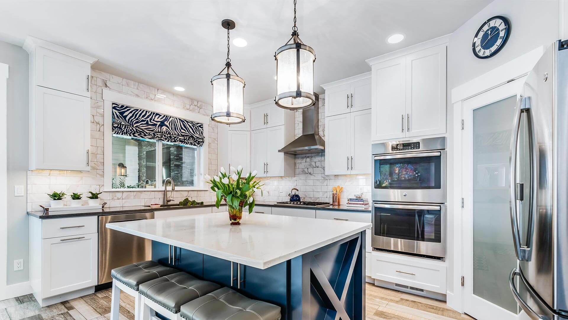 A kitchen with white cabinets , stainless steel appliances , a large island and a clock on the wall.