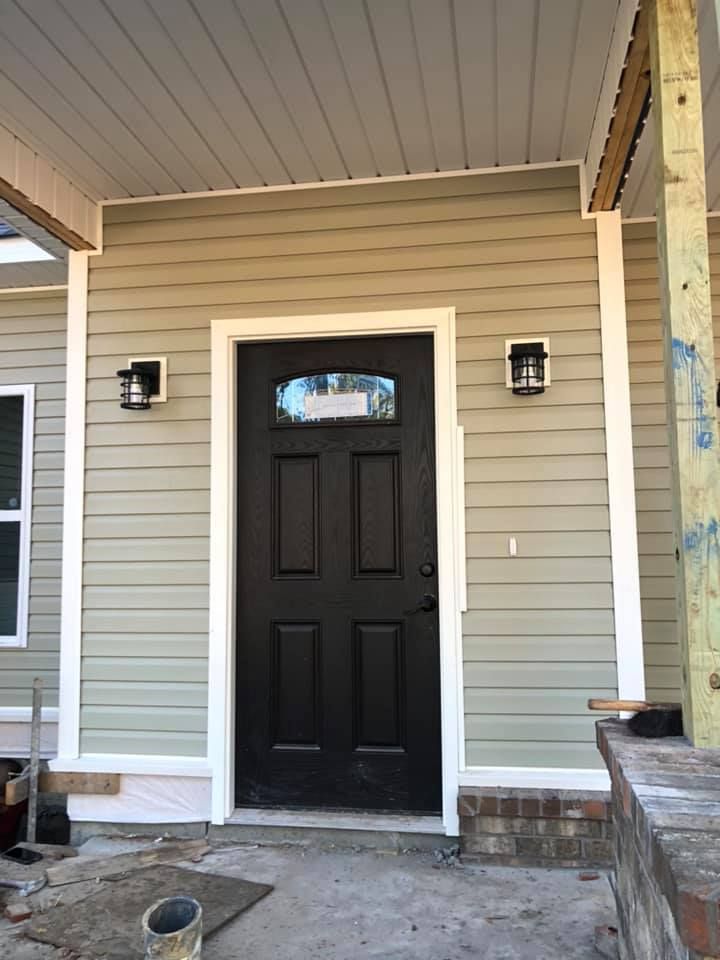 Black front door with sidelights, flanked by sconces on a house with light green siding.