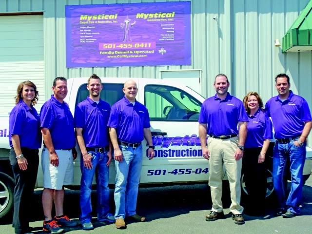 Group of people in purple shirts by a white truck with business sign.