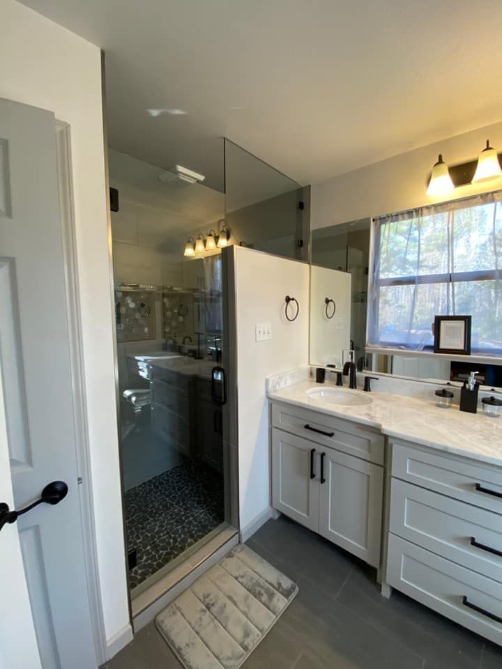Modern bathroom with glass shower, light gray vanity, dark hardware, and gray tile floor.