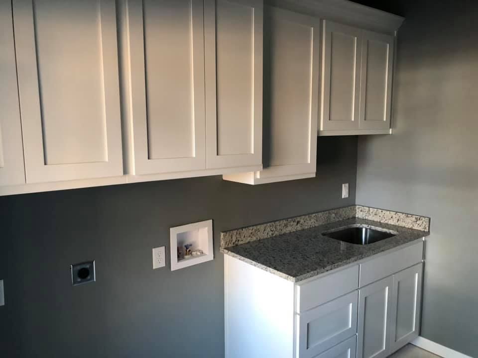 Laundry room with white cabinets, gray walls, granite countertop, and a sink.
