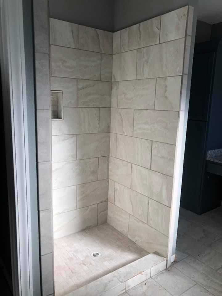 A tiled, walk-in shower with a small recessed shelf and a drain in the floor.