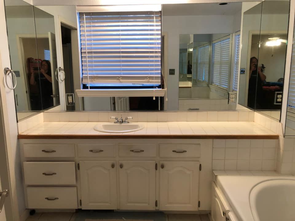 Bathroom with white vanity, cabinets, sink, mirror, blinds, and tub.