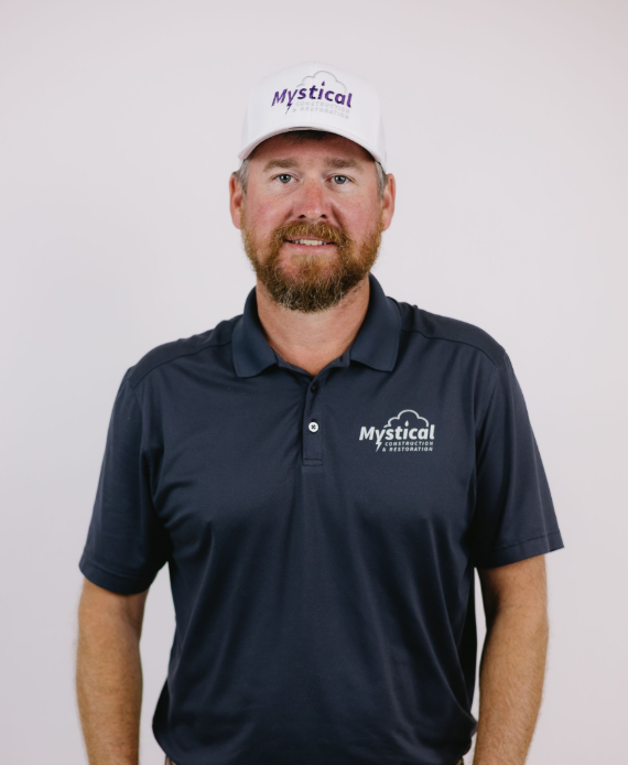 Man in navy polo and white cap with Mystical logo, smiling against a light background