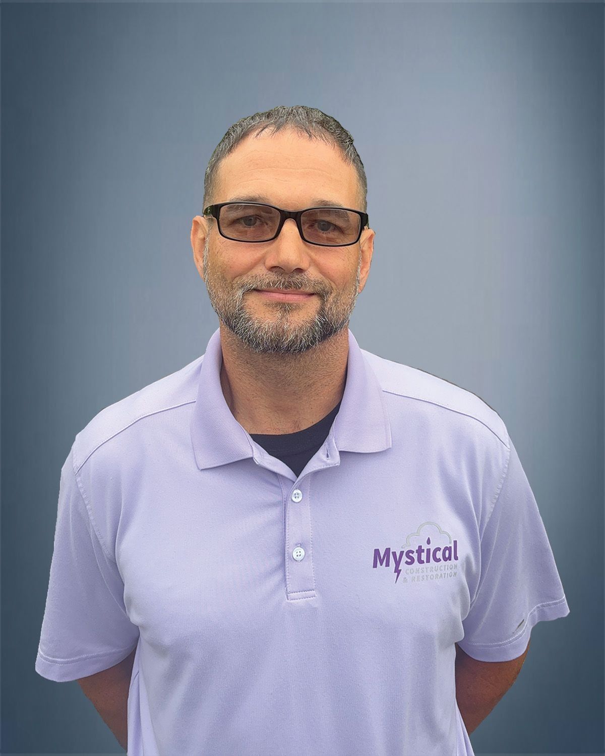 Man wearing glasses and a light purple polo shirt with "Mystical" logo. He's smiling slightly, arms at sides.