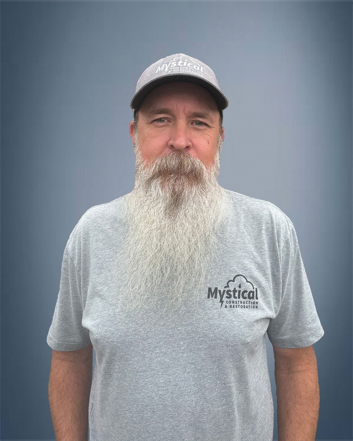 Man with long white beard wearing a baseball cap and gray t-shirt with a logo.