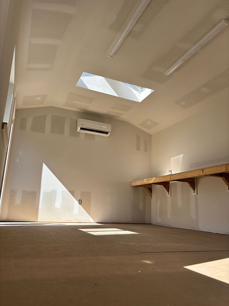 Interior of a light-filled workshop with a skylight, bare drywall, and a workbench along the right wall.