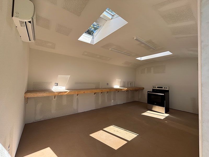 Empty white room with skylights, long work benches, stove and air conditioner.