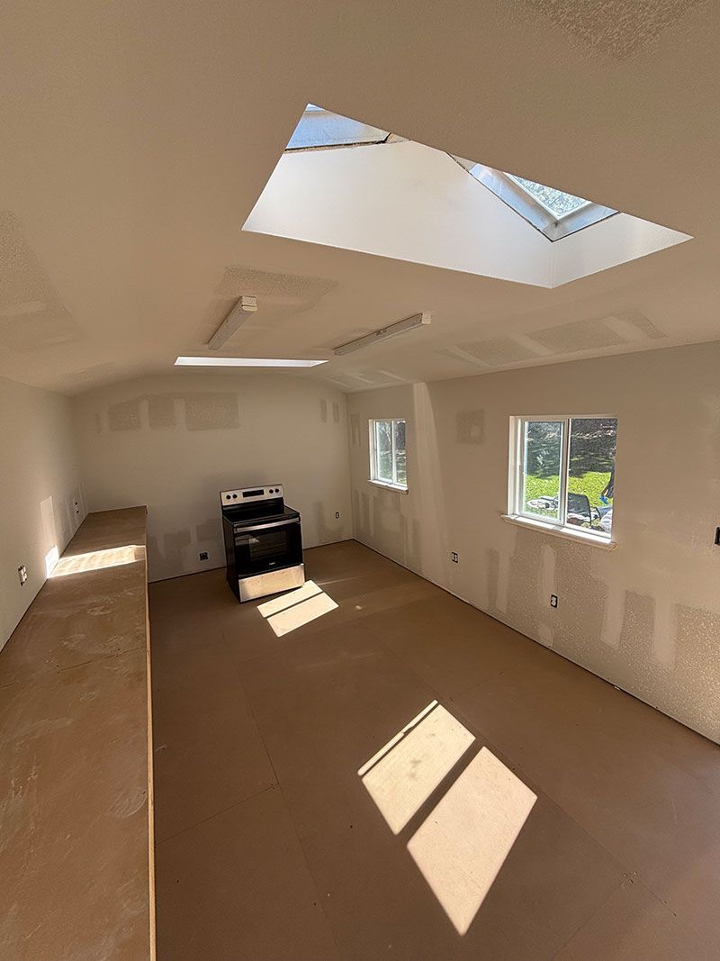 Interior of a room with a stove, skylight, and windows, unfinished walls and floor.