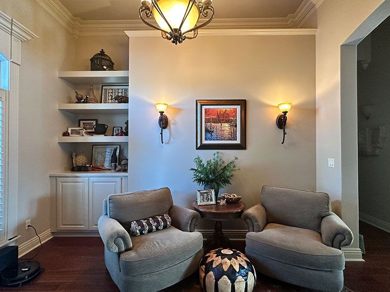 Cozy seating area with two armchairs, a small table, and a built-in shelf unit. Warm lighting and artwork adorn the walls.