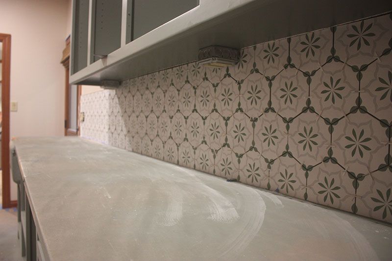 Gray kitchen countertop with patterned tile backsplash and cabinets.