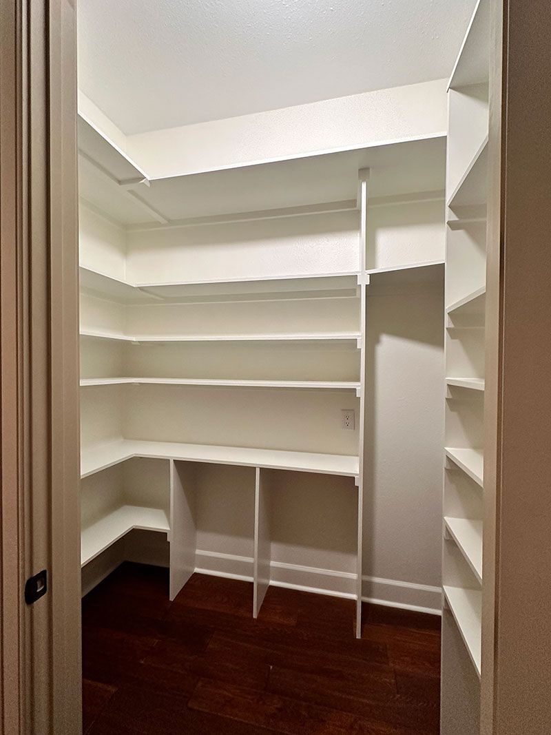 Empty white pantry with multiple shelves. Dark wooden floor.