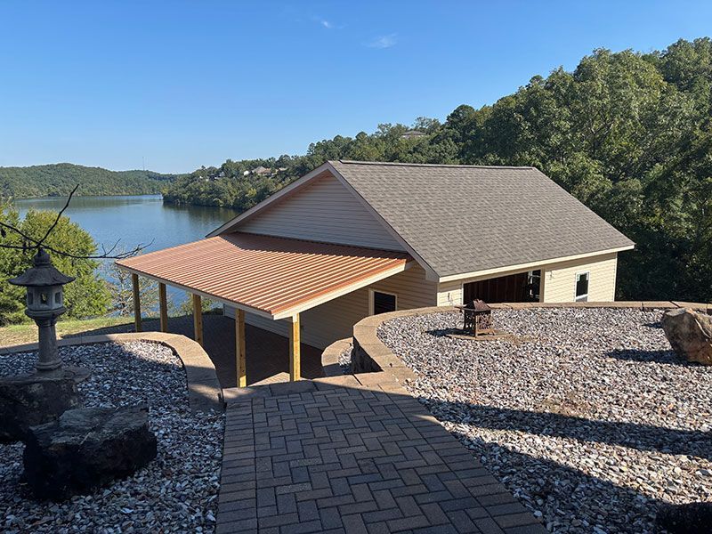 Building with a copper awning overlooking a lake, with stone pathway.