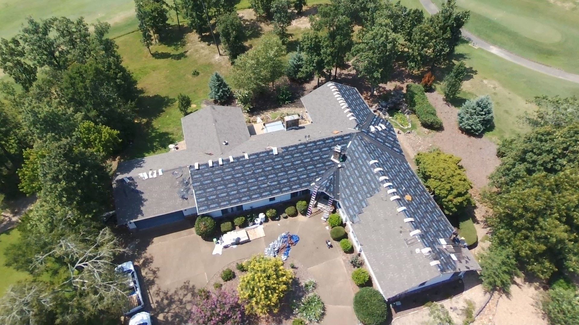 Aerial view of a dark-roofed house surrounded by trees and a golf course.